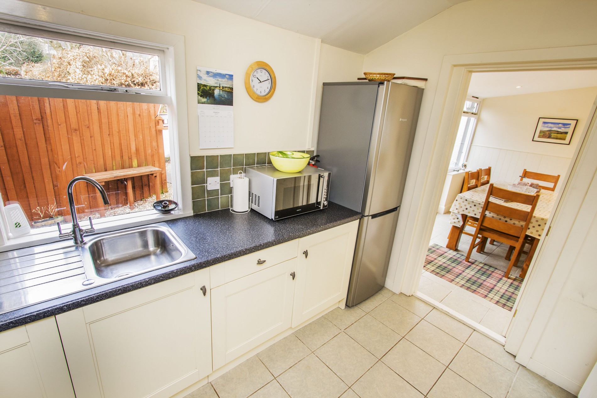 Kitchen with sink, microwave and fridge/ freezer leading to dining room.