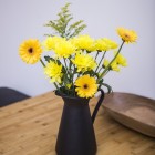 Yellow flowers in a black vase with handle.