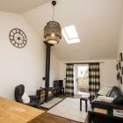 Living room with overhead basket light, clock, large window, sofa, fireplace, TV and an armchair.