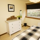 Double bed looking onto white chest of drawers beside long window.
