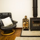 Black armchair next to log stack and a wood burner