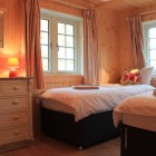Wooden bedroom with two single beds, two windows and a chest of drawers
